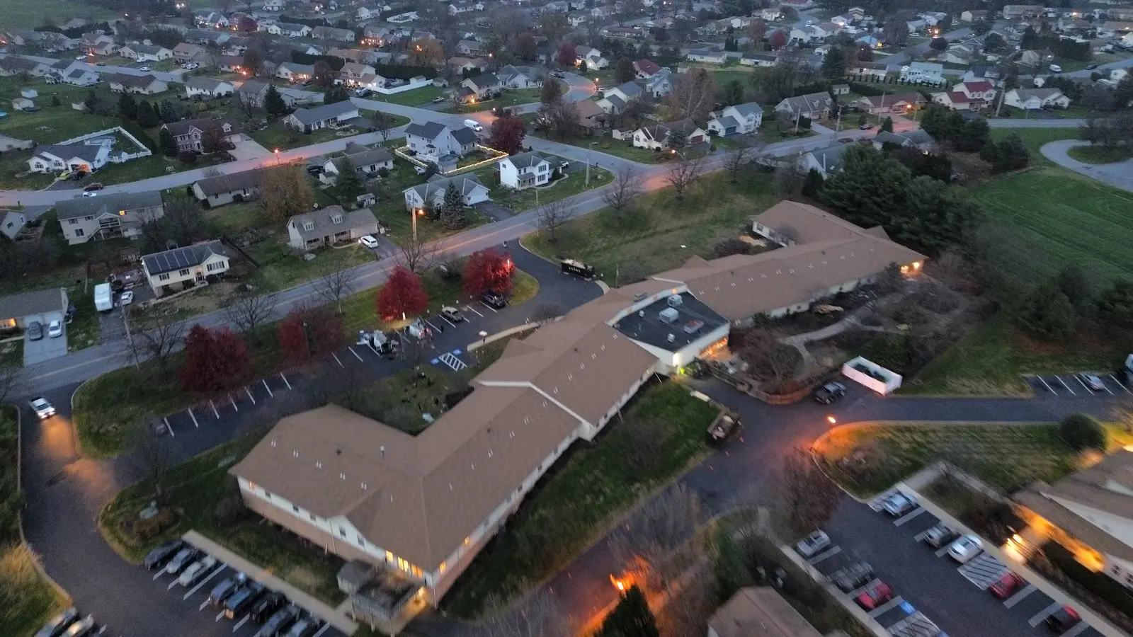 Dusk aerial of the same multi-family building with its finished tan shingle roof and the neighborhood behind it